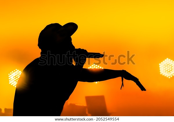 Silhouette of a male singer performing in\
front of a musical equipment red yellow\
colours