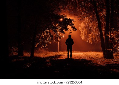 Silhouette Of A Man In An Autumn Foggy Night Park.