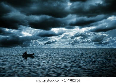 silhouette of a man in a boat floating on the sea. Rich dark clouds. blue tint