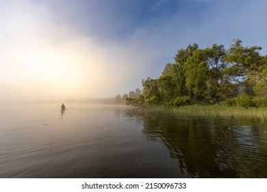 Silhouette of a man in a boat. Mystical landscape. Fog in the early morning on the river. The trees near the water are illuminated by the rays of the rising sun.