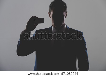 silhouette of man, businessman or manager holding business or bank card in blue formal suit on grey background. Shadow business and economy, banking, fraud, skimming, ecash and information