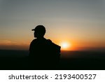 Silhouette of man with cap and backpack contemplating the landscape in the orange light of sunset