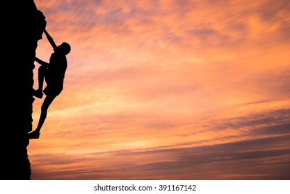 A Silhouette Of Man Climbing On Stone, Mountain At Sunset.