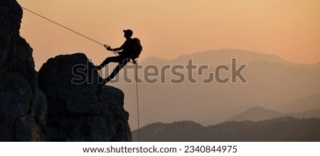 Silhouette of man climbing rock with rope