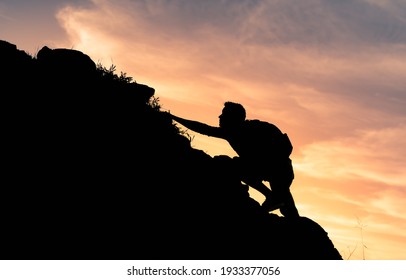 Silhouette of man climbing up steep edge of mountain. 