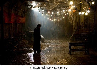 Silhouette of a man in a coat and hat in a dark alley on a rainy night