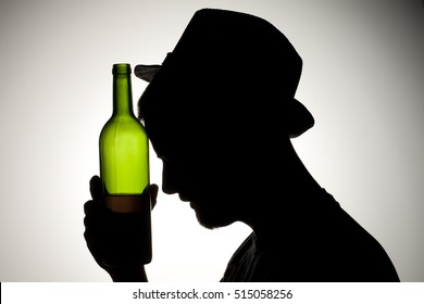 Silhouette of a man drinking wine from the bottle and smoking.  Alcohol and substance abuse concept - Powered by Shutterstock