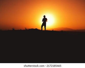 Silhouette Of A Man With Fedora Hat On Sunset On A Hill.