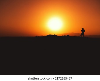 Silhouette Of A Man With Fedora Hat On Sunset On A Hill.