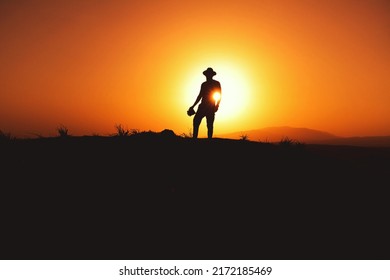 Silhouette Of A Man With Fedora Hat On Sunset On A Hill.