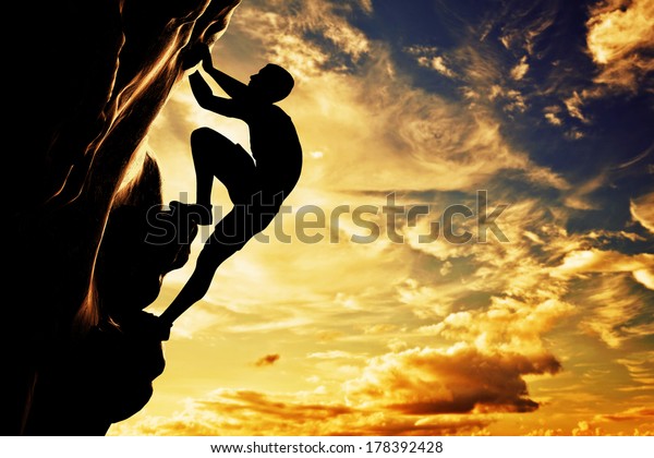 A silhouette of man free\
climbing on rock, mountain at sunset. Adrenaline, bravery,\
leader.