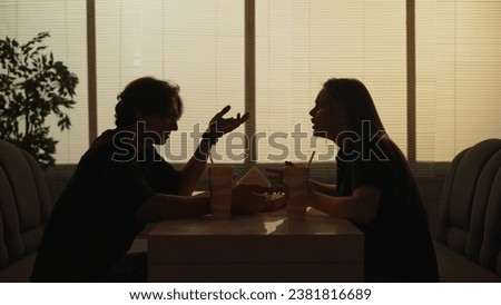 Silhouette of man and girl sitting at the bistro bar talking, arguing, angry face expression tense conversation.