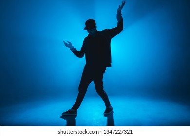 Silhouette Of Man Giving Solo Performance, Dancing Alone In Hip Hop Style On Club Scene With Blue Neon Lightning And Smoke.