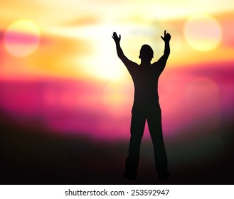 Silhouette of man with hands raised to blurred beautiful sunset background.