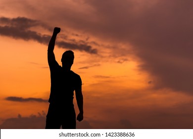 Silhouette of a man with hands raised in the sunset, empowered concept.