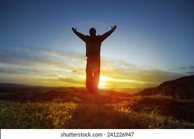 Silhouette of a man with hands raised in the sunset concept for religion, worship, prayer and praise