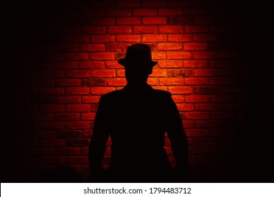 Silhouette Of A Man In A Hat On A Brick Background. Noir, Crime, Detective.