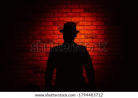 Silhouette of a man in a hat on a brick background. Noir, crime, detective.