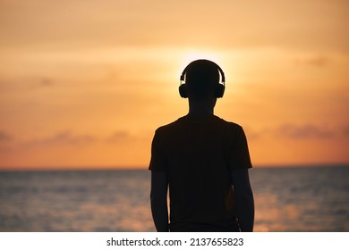 Silhouette Of Man With Headphones Against Ocean. Serenity, Contemplation And Listening Music At Golden Sunset.
