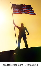 Silhouette Of Man Holding US Flag American On The Mountain. The Concept Of Independence Day. A Successful Silhouette Winner, A Man Waving An American Flag On Top Of A Mountain Peak