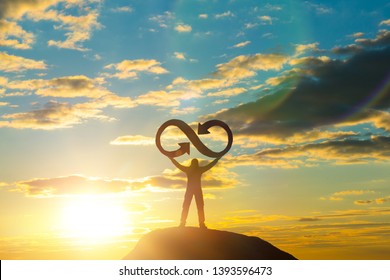 A silhouette of a man holds an infinity symbol on top of a mountain with a sunset background. Concept idea, life, success, business. - Powered by Shutterstock