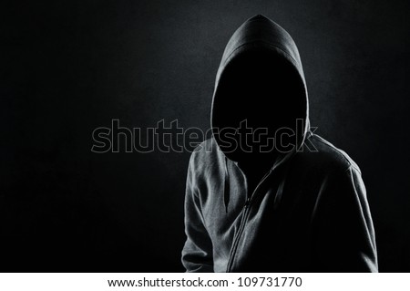 Silhouette of man in the hood or hooligan over dark concrete background with copy space