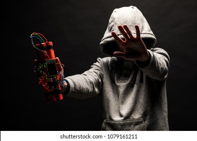 The silhouette of a man in the hood on a black background, his face is not visible, shows hands gesture and a time bomb. The concept of criminal terrorism