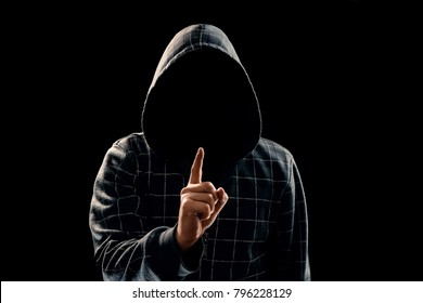 Silhouette of a man in a hood on a black background, his face is not visible, he lifts his finger up. The concept of a criminal, incognito, mystery, secrecy, anonymity. - Shutterstock ID 796228129