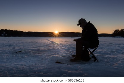 Silhouette Of A Man Ice Fishing On A Lake In Norway At Sunset.