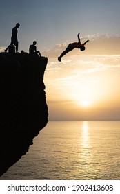A silhouette of a man jumping off a cliff into the ocean at sunset