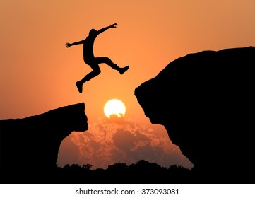 Silhouette of man jumping over cliff on sunset background , business concept