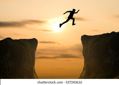 silhouette of man jumping over the cliff on sunset background, business concept idea