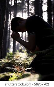 Silhouette Of A Man Kneeling And Praying In The Forest