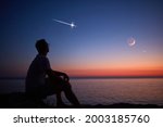 Silhouette of a man looking at the Moon and stars over sea ocean horizon.