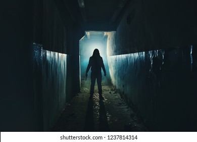 Silhouette of man maniac or killer or horror murderer with knife in hand in dark creepy and spooky corridor. Criminal robber or rapist concept in thriller atmosphere, toned