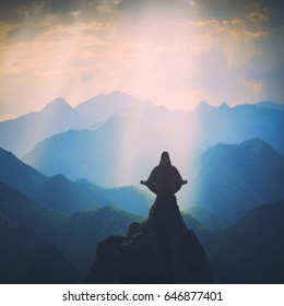 Silhouette Of Man Meditating In Sitting Yoga Position On The Top Of Mountain Above The Misty Valley. Zen, Meditation, Peace. Instagram Stylization.