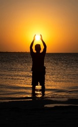 Silhouette Of A Man On The Beach During Sunset Simulating Catching The Sun With His Hands