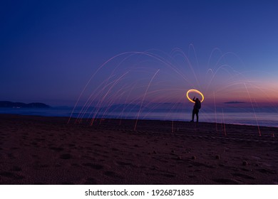 Silhouette of man on the beach making sparks with steel wool. Long exposure light painting photography. Light shapes on the beach at sunset - Powered by Shutterstock