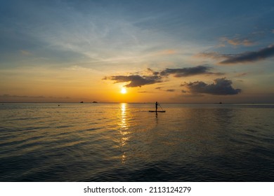 Silhouette of a man on a paddleboard during beautiful sunset on the water of the sea on the island of Koh Phangan, Thailand. Active rest on the sea