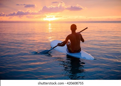 Silhouette of man paddling on paddle board at sunset. Watersport near the beach on sunset