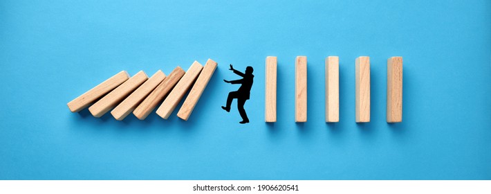 Silhouette of a man in panic against collapsing wooden dominos on blue background. Business crisis and failure concept in wide view. - Shutterstock ID 1906620541