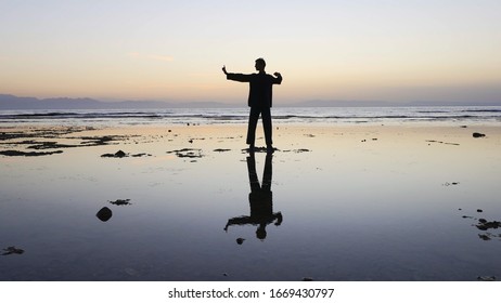 Silhouette of man practiceing qigong exercises at sunset by the sea.