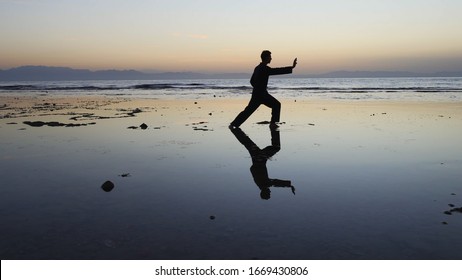 Silhouette of man practiceing qigong exercises at sunset by the sea - Powered by Shutterstock