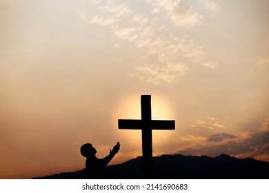 Silhouette of a man prayer in front of cross on mountain at sunset. concept of religion.