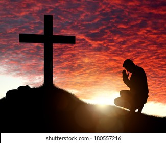 Silhouette of man praying to a cross with heavenly cloudscape sunset concept for religion, worship, love and spirituality