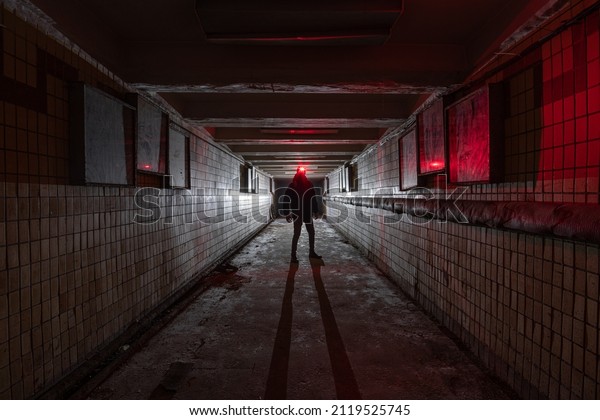 Silhouette of a man\
with a red lantern in dark interior of an abandoned underpass\
tunnel lit by a\
lantern.