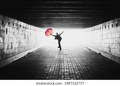 Silhouette of man with red umbrella in a tunnel. Black and white image with light coming from behind. Person jumping towards the camera. Lens facing against the light. - Powered by Shutterstock