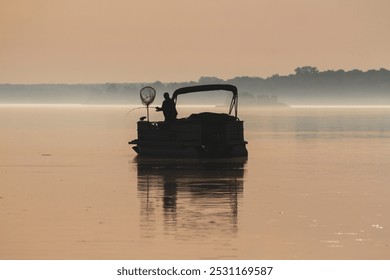 Silhouette of a man reeling in a fish on a pontoon boat during the early morning mist. - Powered by Shutterstock