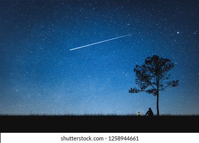 Silhouette of man sitting on mountain and night sky with shooting star. Alone concept. - Shutterstock ID 1258944661