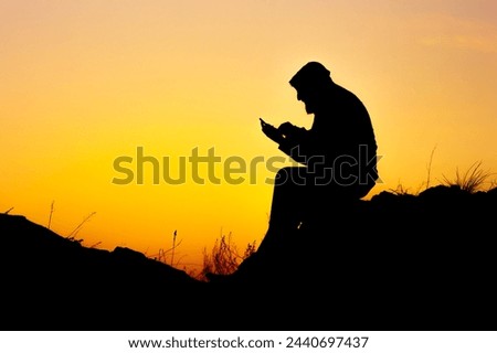 the silhouette of a man sitting on the rocks against the sunset and reading a book. reading smart books against a sunset background